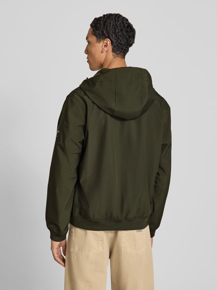 Männermodel trägt Regular Fit Jacke mit Logo-Detail von JACK & JONES in Dunkelgrün, Softshell mit Kapuze und elastischen Abschlüssen, Ganzkörperansicht Rückansicht.