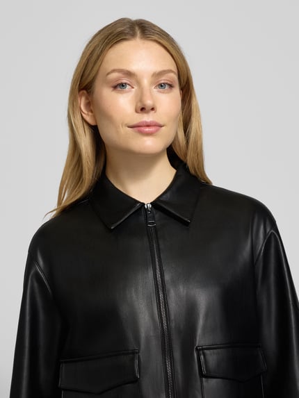 Frauenmodel trägt Jacke in Leder-Optik Modell 'Josmica' von Opus, Regular Fit, Umlegekragen, Reißverschluss, Pattentaschen, Nahaufnahme Oberkörper. Rückenlänge bei Größe 36: 50 cm, Schulterbreite: 48 cm, Brustweite: 53 cm, Ärmellänge: 57 cm.