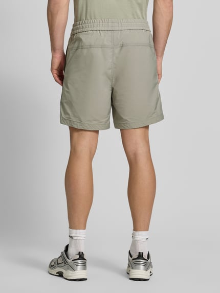 Mężczyznamodel nosi Regular Fit Shorts mit Label-Applikation Modell 'COLAS262S' od HUGO, jednolity kolor, krój regular fit, kontrastowy pasek, elastyczny pas ze sznurkiem, kieszenie boczne. Ganzkörperansicht Rückansicht.