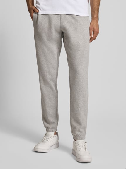 Männermodel trägt Sweatpants mit elastischem Bund von adidas Originals in Grau aus Baumwoll-Mix mit Label-Stitching, Eingrifftaschen, lockerer Schnitt, Ganzkörperansicht von vorne.