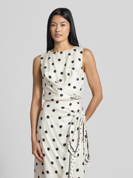 Vrouwenmodel draagt Regular fit blusentop uit zuiver viscose Model 'Veira' van Ted Baker, dames blusentop met mouwloos design en sierblouse, witte stof met zwarte stippen, gladde textuur, ruglengte bij maat 36: 41 cm, mouwlengte bij maat 36: 22 cm. Vooraanzicht bovenlichaam.