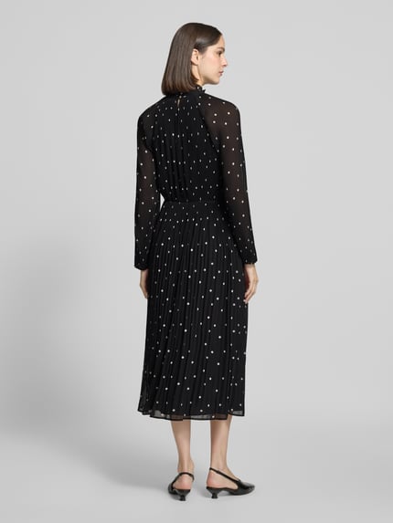Frauenmodel trägt Midikleid im Allover-Look mit Plisseefalten von COMMA, schwarz mit weißen Punkten, A-Linie, Stehkragen, Ganzkörperansicht Rückansicht.