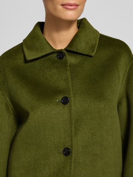 Frauenmodel trägt Jacke aus Lanawoll-Mix mit Knopfleiste Modell 'ALEX' von MANGO in Olivgrün, samtig glatte Textur, Nahaufnahme Oberkörper. Damen Jacke von MANGO, Lanawoll-Mix mit Viskose-Anteil, Regular Fit, Umlegekragen, Knopfleiste.