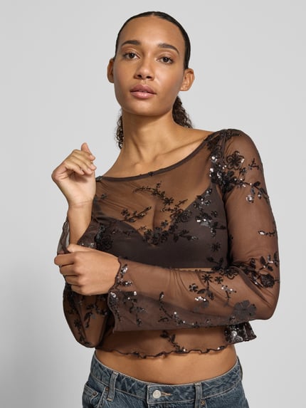 Frauenmodel trägt Langarmshirt mit ausgestelltem Ärmelabschluss von PIECES, transparentes Mesh mit floralem Allover-Spitzenmuster, Nahaufnahme Oberkörper.