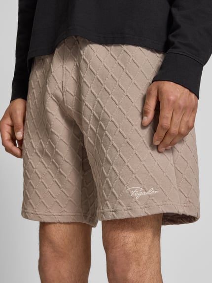 Männermodel trägt Relaxed Fit Shorts mit Strukturmuster Modell 'Jovren' von Pegador in Beige, Elastischer-Material-Mix, Nahaufnahme Oberschenkel, Bundweite 39 cm, Innenbeinlänge 24 cm bei Größe M.
