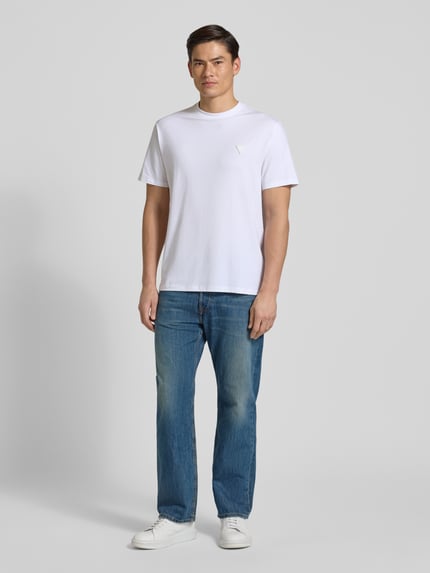 Männermodel trägt T-Shirt mit Logo und Rundhalsausschnitt von Guess, Baumwoll-Mix mit Modal-Anteil, Relaxed-Fit, Rückansicht Ganzkörperansicht von vorne.