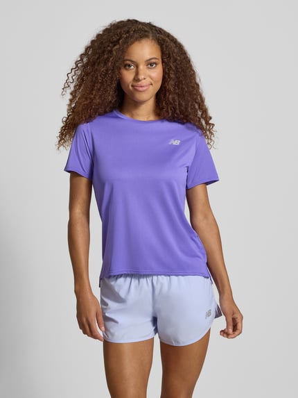 Frauenmodel trägt T-Shirt mit Logo und Rundhalsausschnitt von New Balance in Lila, glatte Textur, Regular Fit, Ganzkörperansicht von vorne.