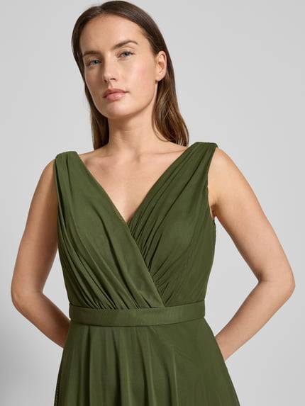 Frauenmodel trägt Cocktailkleid mit V-Ausschnitt von TROYDEN COLLECTION in Oliv, Taillierter Schnitt, Taillengürtel, Nahaufnahme Oberkörper.