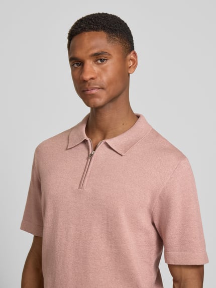 Männermodel trägt Regular Fit Poloshirt mit Reißverschluss Modell 'MILANO' von Jack & Jones Premium in Rosa, Nahaufnahme Oberkörper. Bio-Baumwoll-Mix, Label-Detail.