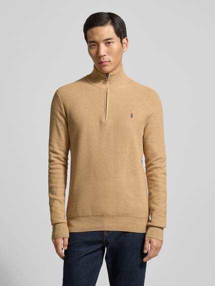 Mężczyzna model nosi Sweter z dzianiny z wyhaftowanym logo od Polo Ralph Lauren, bawełna, krój regular fit, prążkowane wykończenia, stójka, krótki zamek błyskawiczny, długość tyłu 70 cm, długość rękawa 68 cm, beż, gładka tekstura, całkowity widok z przodu.