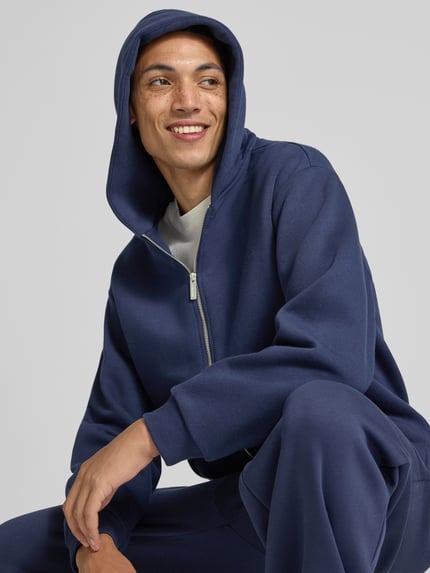 Männermodel trägt Sweatjacke aus Baumwoll-Mix von REVIEW in Dunkelblau, lockere Passform, Nahaufnahme Oberkörper, Context: Kängurutasche, gerippte Abschlüsse, Rückenlänge 70 cm, Ärmellänge 63 cm.