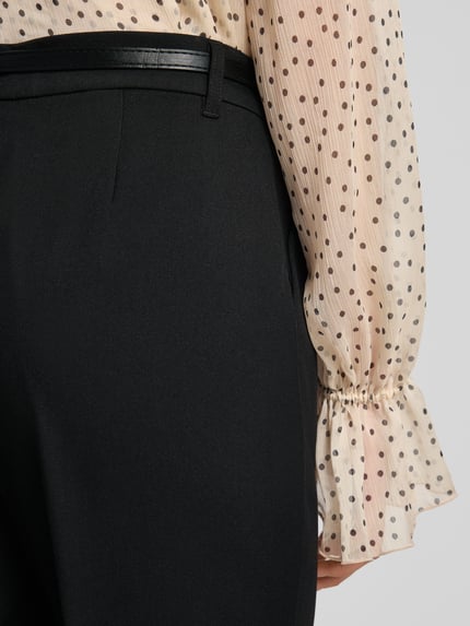 Frauenmodel trägt Barrel Fit Stoffhose mit Gürtel Modell 'ELMA' von Vero Moda in Schwarz, unifarben mit Bundfalten und seitlichen Taschen, Nahaufnahme Rückansicht.