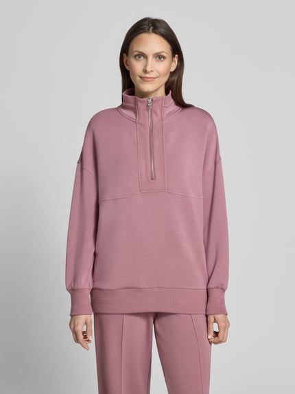 Frauenmodel trägt Damen Sweatshirt mit Troyer-Kragen Modell 'molly' von VARLEY, Viskose-Mix mit Stretch-Anteil, Relaxed-Fit, rosafarbene Oberfläche, kurzer Reißverschluss, überschnittene Schultern, gerippte Ärmelabschlüsse, Ganzkörperansicht von vorne.