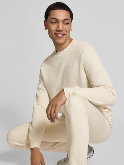 Męski model nosi Regular Fit Sweatshirt mit Logo-Stitching von PUMA PERFORMANCE, mieszanka bawełny, okrągły dekolt, elastyczne wykończenia, kremowy, gładka faktura, Ganzkörperansicht z przodu.