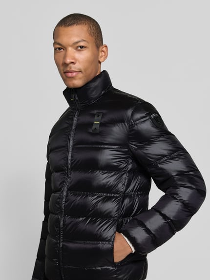 Männermodel trägt schwarze Regular Fit Steppjacke mit Stehkragen Modell 'BELMONT' von Blauer USA, glänzende Textur, Nahaufnahme Oberkörper. Herren Steppjacke, Zweiwege-Reißverschluss, Label-Detail, Rückenlänge 67 cm, Schulterbreite 46 cm, Brustweite 50 cm, Ärmellänge 65 cm.