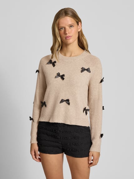 Frauenmodel trägt beigefarbenen Regular Fit Pullover mit Raglanärmeln Modell 'NOELLE' von ONLY, schwarze Schleifendetails, Damen Pullover von ONLY, Ganzkörperansicht von vorne.