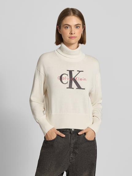 Modelka nosi Regular Fit Pullover aus reiner Baumwolle od Calvin Klein Jeans, kremowy sweter z bawełny, nadruk na przodzie, widok na cały przód, damski kontekst Calvin Klein Jeans.
