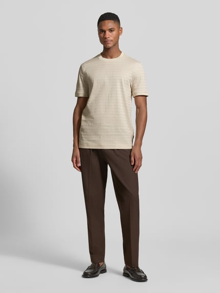 Männermodel trägt Regular Fit T-Shirt aus reiner Baumwolle Modell 'THOMSON' von BOSS in Beige mit feinem Strukturmuster, Ganzkörperansicht von vorne.