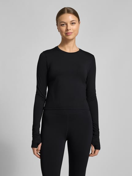 Frauenmodel trägt Slim Fit Longsleeve mit Rundhalsausschnitt Modell 'Feather' von Fabletics, elastischer Material-Mix, schwarz, Ganzkörperansicht von vorne.