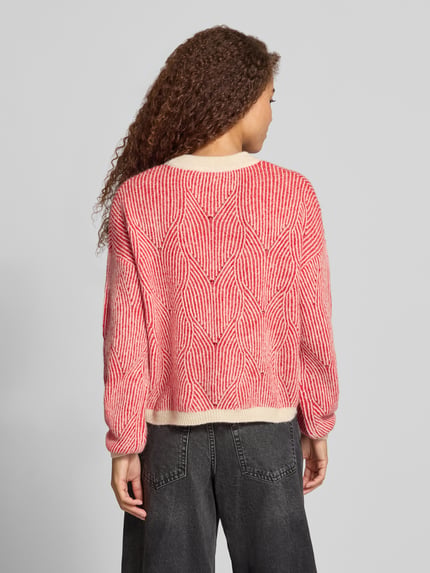 Frauenmodel trägt Pullover mit strukturiertem Jacquard-Strick von PIECES in Rot und Creme, geometrisches Allover-Muster, Strickoptik, Ganzkörperansicht Rückansicht.