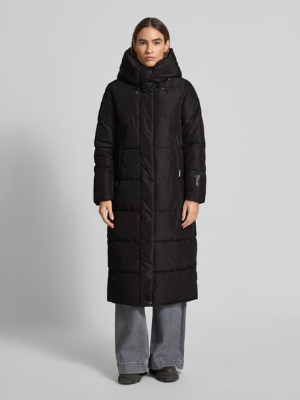 Vrouwenmodel draagt zwarte Steppmantel met Stehkragen Modell 'Soulani' van khujo, rechte snit, lange mouwen, voorkant geheel zichtbaar, Ganzkörperansicht von vorne.