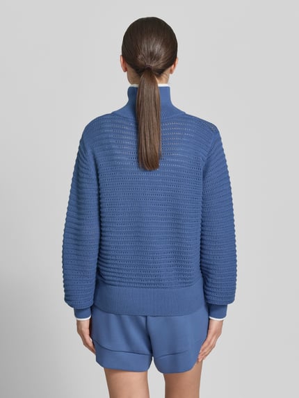 Vrouwenmodel draagt gebreide pullover met ritssluiting model 'morwenna' van VARLEY, puur katoen, regular fit, opstaande kraag, ruglengte maat S 61 cm, mouwlengte maat S 76 cm, dames, blauwe kleur, gestructureerd breisel, gemengde texturen, volledige rugaanzicht.