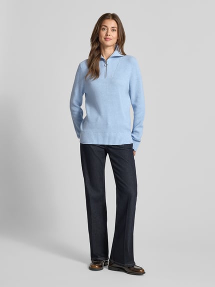 Frauenmodel trägt Regular Fit Strickpullover aus Viskose-Mix von Christian Berg Woman in Hellblau mit Troyer-Kragen, gerippten Abschlüssen und langen Ärmeln, kombiniert mit dunkler Hose; Ganzkörperansicht von vorne. Rückenlänge Größe S: 61 cm, Ärmellänge: 69 cm.