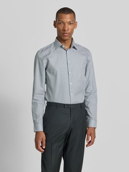 Männermodel trägt Slim Fit Business-Hemd mit Kentkragen von Jake*s, weiße und blaue Streifen, Reine Baumwolle, Knopfleiste, Sportmanschetten, abgerundeter Saum, Rückenlänge 78 cm, Schulterbreite 47 cm, Ärmellänge 66 cm, Ganzkörperansicht von vorne.