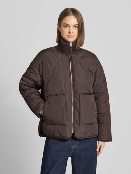 Frauenmodel trägt Steppjacke mit gestricktem Stehkragen Modell 'SERENA' von JJXX in Dunkelbraun, große Flächensteppung, Loose Fit, Ganzkörperansicht von vorne.