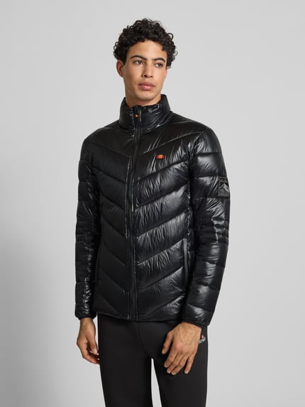 Männermodel trägt schwarze Steppjacke mit Stehkragen Modell 'ORSINI' von Ellesse, Label-Details, Ganzkörperansicht von vorne