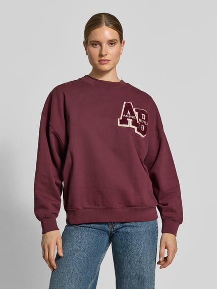 Modelka nosi Oversized Sweatshirt aus Baumwolle od Anine Bing, bordowy kolor, okrągły dekolt, naszywka z logo, długie rękawy, elastyczne wykończenia, długość tyłu w rozmiarze S: 61 cm, bawełna, widok całej sylwetki z przodu.