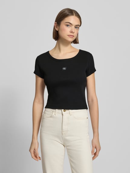 Vrouwenmodel draagt Cropped T-shirt met Labeldetail van Calvin Klein Jeans, zwarte kleur, mix van katoen en elastaan, ronde hals, korte look, ruglengte maat S 43 cm, Ganzkörperansicht von voren.