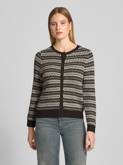 Frauenmodel trägt Cardigan mit Zierknöpfen von VERO MODA, geometrisches Allovermuster, Strickoptik, Rundhals, Langarm, Vorderansicht, Nahaufnahme Oberkörper.