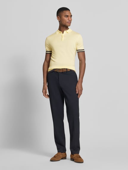 Männermodel trägt Slim Fit Poloshirt aus Lyocell-Seide-Mix von Guess Modell 'LARRY' mit Polokragen, Knopfleiste, Kontraststreifen, Ganzkörperansicht von vorne.