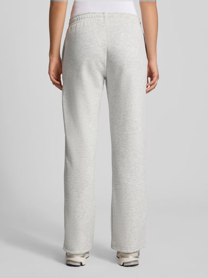 Frauenmodel trägt Wide Fit Sweatpants aus Baumwoll-Mix Modell 'Iconic' von Gina Tricot in Hellgrau, elastischer Bund, Ganzkörperansicht Rückansicht. Damen Sweatpants, Baumwoll-Mix, elastischer Bund mit Tunnelzug, Innenbeinlänge ca. 80 cm bei Größe S.