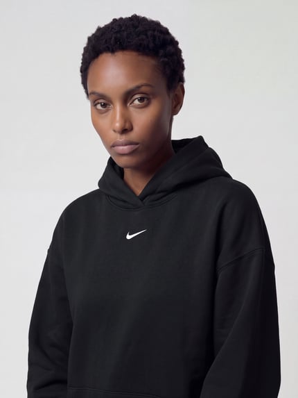 Frauenmodel trägt Oversized Fit Hoodie aus reiner Baumwolle von Nike, unifarben schwarz, Strukturmuster, Logo-Detail, Nahaufnahme Oberkörper.