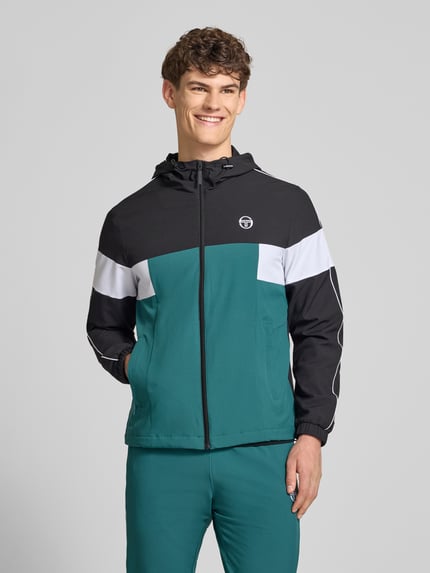 Męski model nosi Regular Fit Jacke mit Logo-Stitching Modell 'Caspio' od SERGIO TACCHINI w zielono-czarno-białych kolorach, krój regular fit, kaptur z tunelem, zamek błyskawiczny, kieszenie, elastyczne mankiety, długość tyłu 70 cm, długość rękawa 68 cm, widok całej sylwetki z przodu