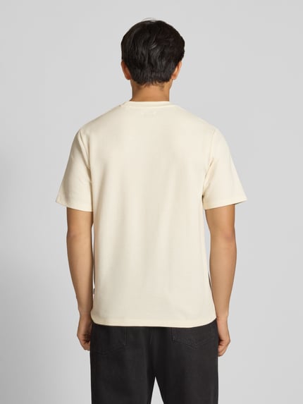 Mężczyznamodel nosi męski t-shirt o kremowym kolorze, prosty krój, elastyczna mieszanka materiałów z bawełną, model 'AUSTIN' od Jack & Jones, stójka, długość tyłu w rozmiarze M: 70 cm, całkowity widok z tyłu.