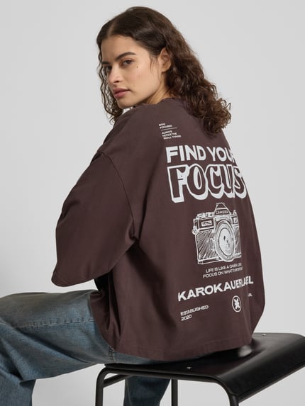 Frauenmodel trägt Oversized T-Shirt mit Rundhalsausschnitt von Karo Kauer, braune Baumwolle, Label-Print, Rückenansicht, Nahaufnahme Oberkörper.