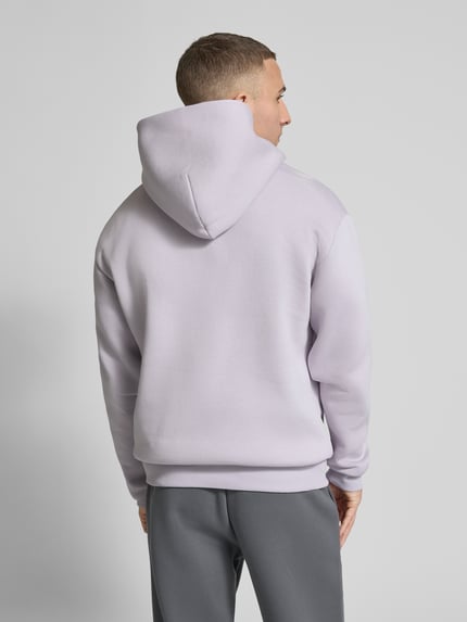 Männermodel trägt Hoodie mit Känguru-Tasche von REVIEW, mieszanka bawełny, luźny krój, kaptur, detal z logo, kieszeń kangurka, elastyczne wykończenia, długość tyłu w rozmiarze M: 68 cm, długość rękawów w rozmiarze M: 62 cm, jasnofioletowy, proste faktury, Ganzkörperansicht Rückansicht.