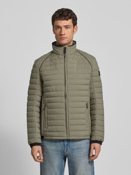 Männermodel trägt Steppjacke mit Stehkragen und Reißverschlusstaschen von NAUTGÅRD in khaki, Regular-Fit, Ganzkörperansicht von vorne. Kontext: Rückenlänge bei Größe M 69 cm, Schulterbreite 40 cm, Brustweite 46 cm, Ärmellänge 62 cm.