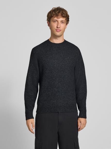 Männermodel trägt Strickpullover mit Logo-Stitching Modell 'CURTIS' von Carhartt Work In Progress, dunkle Farbe, lockerer Schnitt, Ganzkörperansicht von vorne.