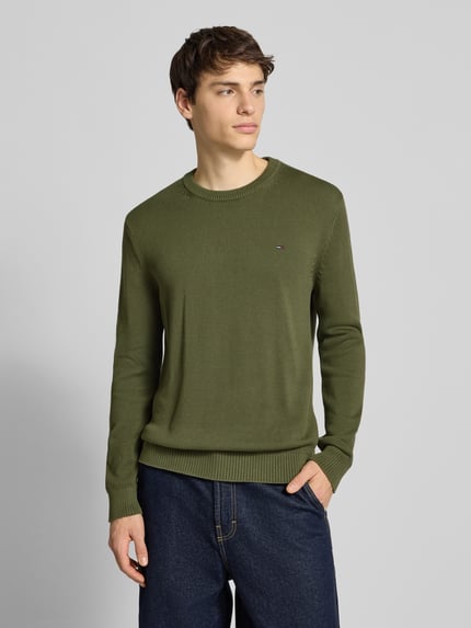 Männermodel trägt Regular Fit Strickpullover aus reiner Baumwolle von Tommy Jeans in Olivgrün, unifarben, Nahaufnahme Oberkörper.