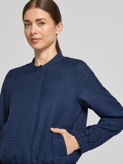 Vrouwenmodel draagt Regular Fit blouson met baseballkraag model 'MELANEY' van Vero Moda, mêlee look, zij-steekzakken, lange mouw, geribde rompzoom, drukknoopsluiting. Nahaufnahme bovenlichaam.