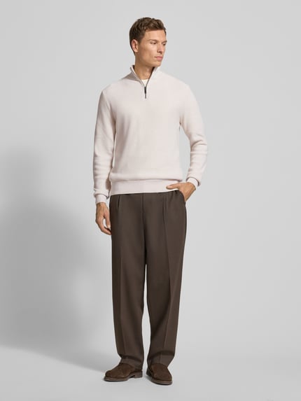 Męski model nosi Strickpullover mit Stehkragen od MCNEAL z bawełny, slim fit, jasny kolor, brązowe spodnie, widok całej sylwetki z przodu.
