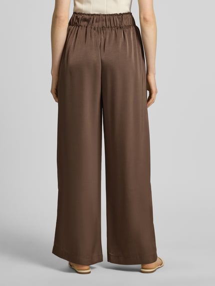 Männermodel trägt spodnie materiałowe Wide Leg Stoffhose aus Baumwoll-Mix Modell 'LUCA' von VILLA SOPHIE, efekt: jednolity kolor, krój: spodnie z szerokimi nogawkami, aplikacja: naszywka z logo, ściągacz: elastyczny, wpuszczane kieszenie, mieszanka bawełny; Ganzkörperansicht Rückansicht.