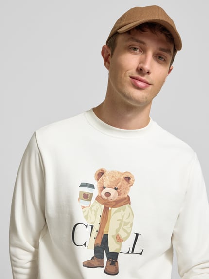 Męski model nosi Sweatshirt mit Motiv-Print von CHILL PILL, bawełniana mieszanka, krój regular fit, nadruk z motywem, okrągły dekolt, długość tyłu w rozmiarze M 70 cm, długość rękawa 67 cm, jasne kolory, prosty fason, miękka tekstura, zbliżenie na górną część ciała.