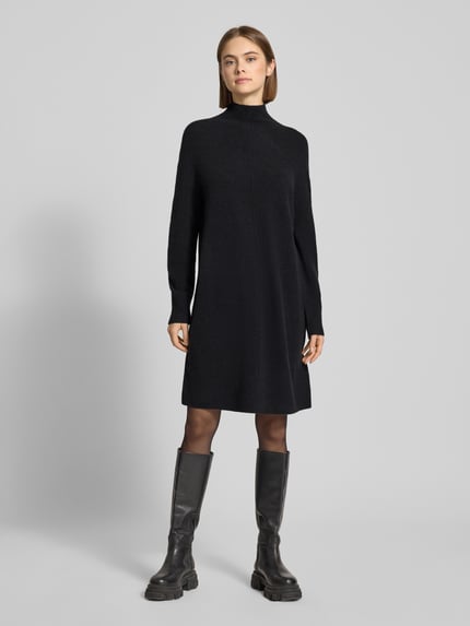 Frauenmodel trägt Oversized Strickkleid aus Schurwoll-Mix von Marc O'Polo Denim, unifarben in Schwarz, Mini-Länge, hochgeschlossen, gerippte Ärmelabschlüsse und Saum, lockere Passform, Stricktextur, Ganzkörperansicht von vorne.