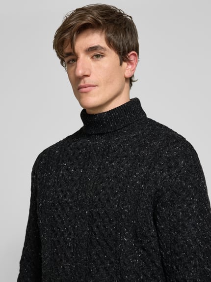 Männermodel trägt Rollkragenpullover mit Zopfmuster-Struktur von Selected Homme in schwarzer Strickoptik mit Melange, Nahaufnahme Oberkörper.