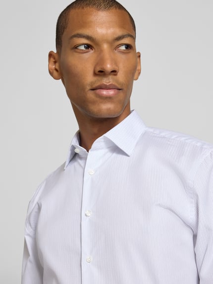 Männermodel trägt Slim Fit Businesshemd in Premiumqualität von Jake*s in Weiß mit feinen Streifen, Nahaufnahme Oberkörper.